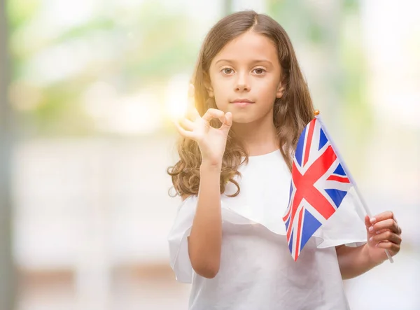 優秀なシンボルの指で サインをしているイギリスの旗を保持しているブルネットのヒスパニック系少女 — ストック写真