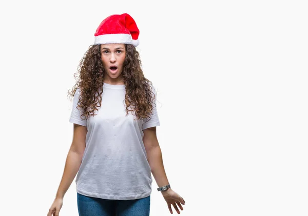 年轻的黑发女孩戴着圣诞帽在孤立的背景恐惧和震惊与惊喜的表情 恐惧和兴奋的脸 — 图库照片