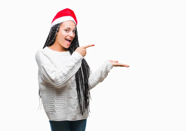 年轻的编织头发非洲裔美国女孩戴着圣诞节帽在孤立的背景惊讶和微笑的相机 而呈现与手和手指指指点点 — 图库照片