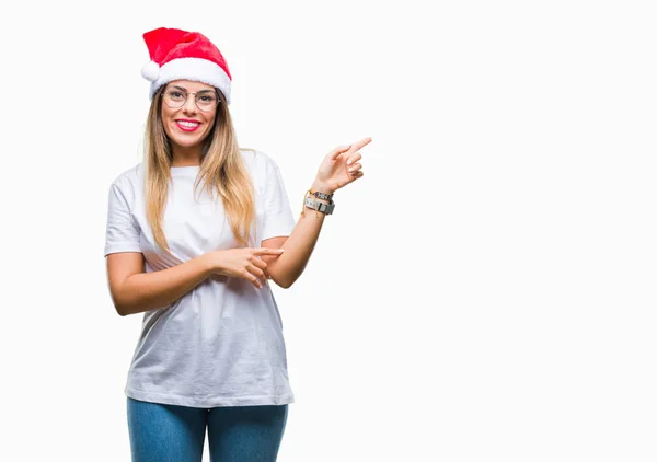 若くてきれいな女性の顔に大きな笑みを浮かべて隔離された背景にクリスマスの帽子を着てカメラを見て側の手と指で指す — ストック写真