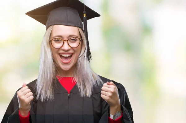 孤立した背景を祝う以上大学院制服を着て若いブロンドの女性は驚きし びっくりの腕の成功のため調達と開いた目 勝者の概念 — ストック写真