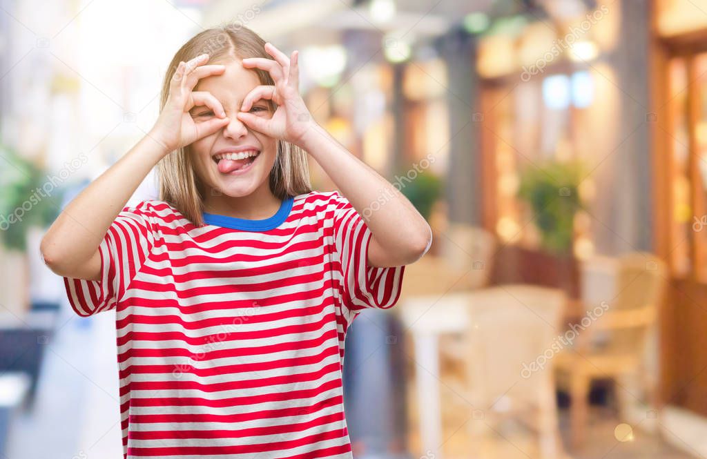 Young beautiful girl over isolated background doing ok gesture like binoculars sticking tongue out, eyes looking through fingers. Crazy expression.