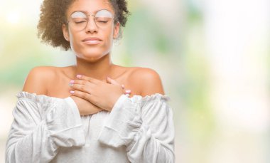 Göğüs kapalı gözler ve yüzünde minnettar jest ile genç afro Amerikalı kadın gözlük ile gülümseyen izole arka plan üzerinde eller. Sağlık kavramı.