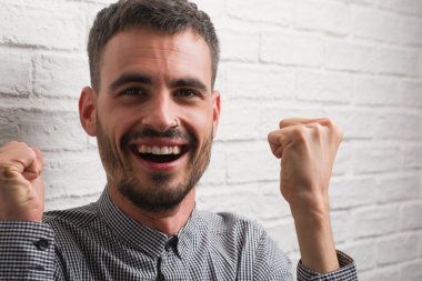 Duygu tezahürat genç yetişkin adam gurur çığlık ve zafer ve başarı çok heyecanlı, kutluyor beyaz tuğla duvarı ayakta