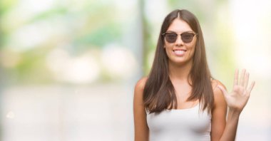 Beş kendinden emin ve mutlu gülümseyerek sırasında gösterilen ve parmakları ile işaret genç güzel İspanyol giyen güneş gözlüğü numara.