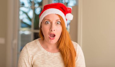 Santa claus şapka bir sürpriz yüz, korkuyor ve heyecanlı korku ifadesi ile şok korkmuş giyen kızıl saçlı kadın