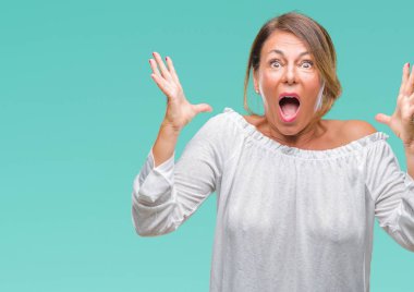 Orta yaş üst düzey İspanyol kadın deli kutluyor arka plan izole ve başarı için kaldırdı kollarını açarak hayrete ve heyecanlı çığlık gözleri açık. Kazanan kavramı