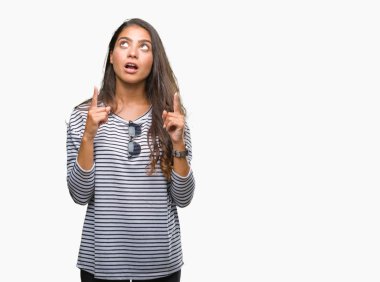 Genç güzel Arap kadın hayrete ve yukarıya bakıyor ve parmakları ile işaret ve silah kaldırdı sürpriz izole arka plan üzerinde güneş gözlüğü takıyor.