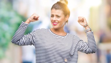 Genç güzel kadın rahat kazak kol kasları gururlu gülümseyen gösterilen izole arka plan üzerinde çizgili. Fitness kavramı.