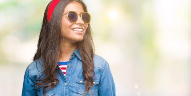 Genç güzel Arap kadın uzak tarafına yüzünde, doğal ifade gülümseme ile seyir izole arka plan üzerinde güneş gözlüğü takıyor. Kendine güvenen gülüyor.