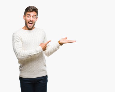 Hayret ve el ile sunulması ve parmak ile işaret ederken kameraya gülümseyen izole arka plan üzerinde kış kazak giyen genç yakışıklı adam.