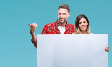 Genç çift birlikte holding boş afiş işaret ve başparmak kadar mutlu yüz gülümseyen tarafı ile gösteren izole arka plan üzerinde