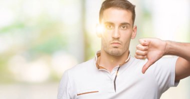 Kızgın yüz, eksi işareti aşağı antipati başparmak ile gösterilen, ret kavramı ile beyaz t-shirt giyiyor rahat yakışıklı genç