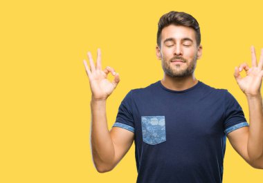 Yakışıklı delikanlı izole arka plan üzerinde dinlenmek ve gülümseyen gözlerle parmak ile meditasyon jest yapıyor kapalı. Yoga kavramı.