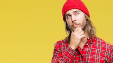 Genç yakışıklı adam uzun saçlı çene düşünme hakkında soru, dalgın ifade üzerine el ile izole arka plan üzerinde kırmızı şapkası. Düşünceli yüzüyle gülümsüyor. Şüphe kavramı.