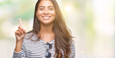 Genç güzel Arap kadın ve kendinden emin ve mutlu gülümseyerek süre parmak numaralı yukarıyı gösteren izole arka plan üzerinde güneş gözlüğü takıyor.