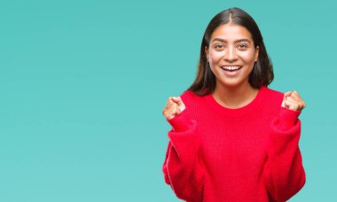 İzole arka plan üzerinde kutluyor kış kazak giyen genç güzel Arap kadın şaşırttı ve başarı için kaldırdı kollarını açarak hayret ve gözleri açık. Kazanan kavramı.