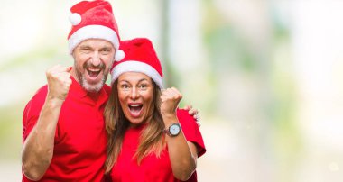 Orta yaş İspanyol çift üzerinde Noel şapka arka plan çok mutlu ve heyecanlı gülümseyen ve başarı için çığlık kaldırdı, silah ile kazanan jest yapıyor izole. Kutlama kavramı.
