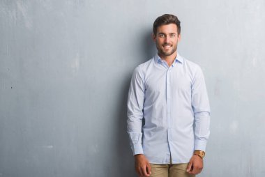 Yakışıklı genç iş adamı yüzünde mutlu ve güzel bir gülümseme ile şık gömlek giymiş gri grunge duvarın üzerinden. Şanslı kişi.