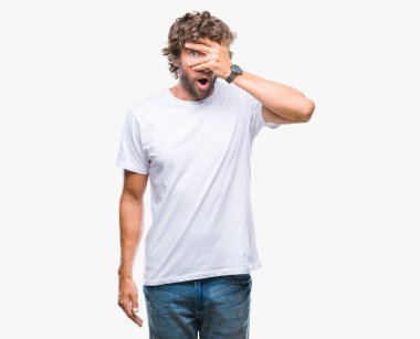 Mahcup ifadeyle parmaklarımın arasından görünen yüz ve gözler el ile kapsayan şok izole arka plan bakmak üzerinde yakışıklı İspanyol modeli adam.