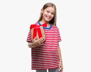 Genç güzel kız Noel ya da Sevgililer hediye izole arka plan üzerinde duran ve diş gösterilen kendine güvenen bir gülümsemeyle gülümseyerek mutlu bir yüz ile vermek