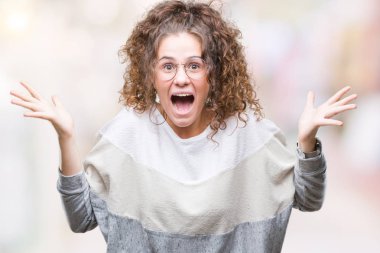 Güzel esmer kıvırcık saçlı Genç kız üzerinde gözlük takan deli kutluyor arka plan izole ve çığlık kaldırdı ve açık gözleri heyecanlı silah ile başarı için hayrete düşürdü. Kazanan kavramı