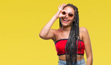 Genç örgülü saç Afrika kökenli Amerikalı üzerinde güneş gözlüğü takıyor Doğum işareti ile gülümseyen, parmakları ile mutlu yüz üzerinden seyir göz el ile ok jest yapıyor arka plan izole.