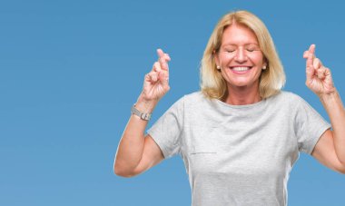 Orta yaş sarışın kadın geçiş parmakları umut ve gözler gülümseyen izole arka plan yüzünden kapalı. Şans ve batıl kavramı.