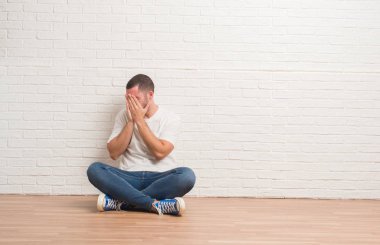 Üzgün ifadeyle yüz eller ile ağlayarak süre kapsayan beyaz tuğla duvarın üzerinden katta oturan beyaz delikanlı. Depresyon kavramı.