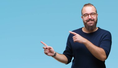 Gülümseyen ve iki elleri ve parmakları ile tarafına işaret kamera bakarak izole arka plan üzerinde güneş gözlüğü takmış Genç beyaz hipster adam.