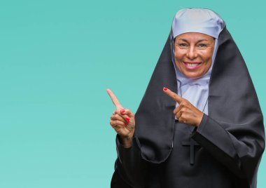 Orta yaş üst düzey Hıristiyan Katolik Rahibe kadın gülümseyerek ve iki elleri ve parmakları ile tarafına işaret kamera bakarak izole arka plan.