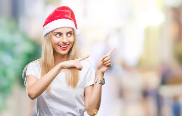 笑顔で側に つの手と指で指しているカメラを見て孤立の背景に若い金髪美人クリスマス帽子 — ストック写真