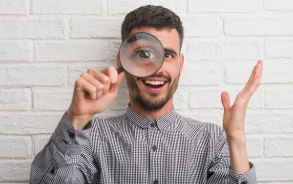 Ung Vuxen Man Över Tegelvägg Med Förstoringsglas Mycket Glad Och — Stockfoto