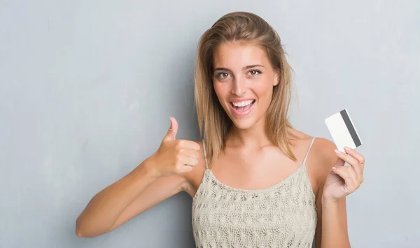 Hermosa Mujer Joven Sobre Pared Gris Grunge Celebración Tarjeta Crédito —  Fotos de Stock