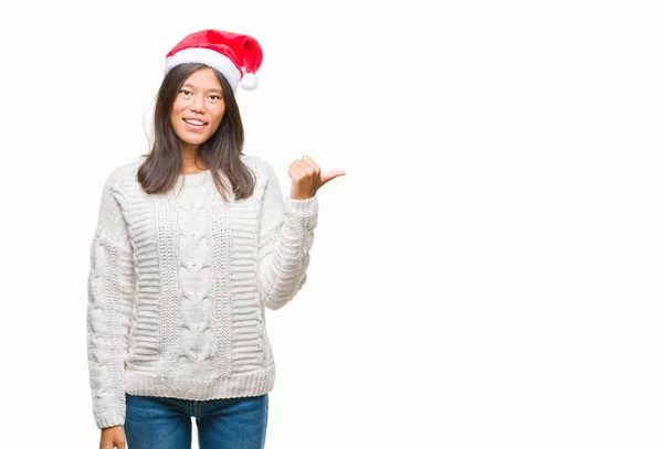 年轻的亚洲妇女戴着圣诞节帽子在孤立的背景微笑与快乐的脸看和指向侧与拇指向上 — 图库照片