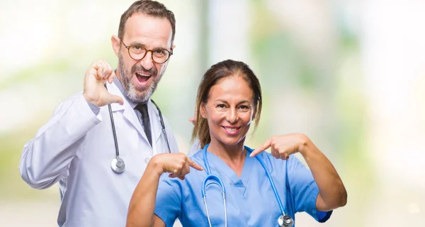 中年西班牙医生伴侣夫妇穿着医疗制服在孤立的背景看起来自信的脸上微笑 用手指自豪和快乐指着自己 — 图库照片