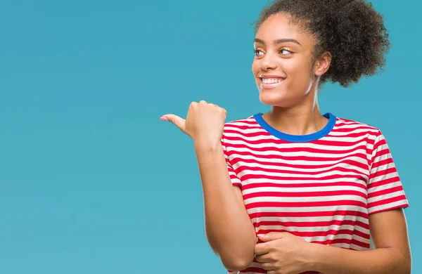 Young afro american woman over isolated background smiling with happy face looking and pointing to the side with thumb up.