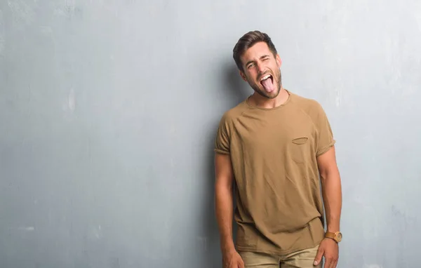 英俊的年轻人在灰色的垃圾墙上伸出舌头 高兴地用滑稽的表情 情感概念 — 图库照片