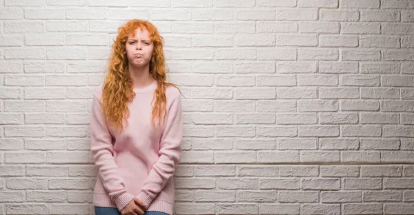 Komik surat ile yanakları şişirme tuğla duvarın üzerinden duran genç Kızıl saçlı kadın. Ağız ile hava, deli ifade şişirilmiş.