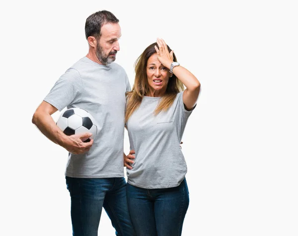 Middle age hispanic couple holding football soccer ball over isolated background with happy face smiling doing ok sign with hand on eye looking through fingers
