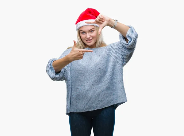 若い白人女性が笑顔の幸せそうな顔で指と手作りフレーム分離の背景にクリスマス帽子をかぶっています 創造性と写真のコンセプト — ストック写真