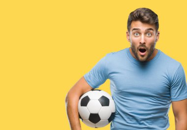 Yakışıklı delikanlı futbol futbol topu izole arka plan üzerinde bir sürpriz yüz, korkuyor ve heyecanlı korku ifadesi ile şok korkmuş holding