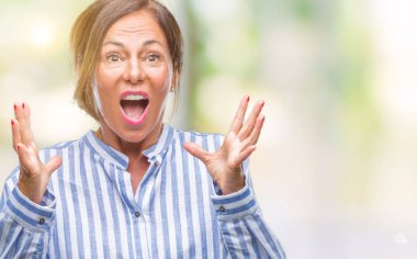 Orta yaş üst düzey İspanyol kadın deli kutluyor arka plan izole ve başarı için kaldırdı kollarını açarak hayrete ve heyecanlı çığlık gözleri açık. Kazanan kavramı