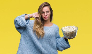 Genç güzel sarışın kadın kızgın yüzü, eksi işareti aşağı antipati başparmak ile gösterilen, ret kavramı ile izole arka plan üzerinde patlamış mısır yemek