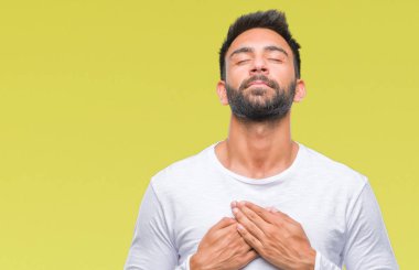 Göğüs kapalı gözler ve yüzünde minnettar jest ile yetişkin İspanyol adam ile gülümseyen izole arka plan üzerinde eller. Sağlık kavramı.