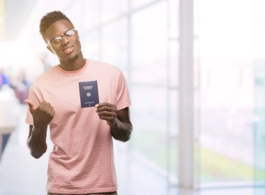 Alman pasaportu el ve parmak ile yukarı dönük ile gülümseyen mutlu yüz tutan genç Afro-Amerikan adam