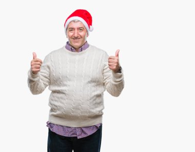 Üst düzey yakışıklı Noel şapka izole arka plan başarı işareti el ile pozitif jest yapıyor üzerinde başparmak gülümseyen ve mutlu. Neşeli bir ifadeyle, kazanan jest kameraya bakıyor.