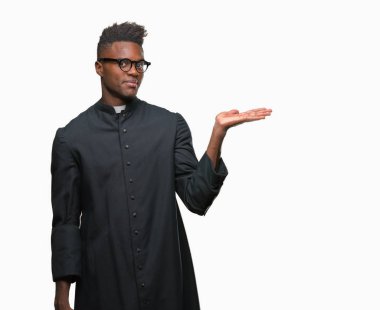 Genç Afro-Amerikan rahip adam neşeli sunulması ve kameraya bakarak avucunun ile işaret gülümseyen izole arka plan.