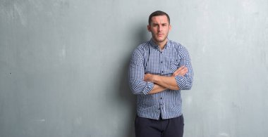 Gri grunge duvar şüpheci ve sinir, onaylamayan ifade yüz çapraz kolları olan genç beyaz adam. Negatif kişi.