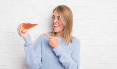 Güzel ve genç birbayan pizza yemek beyaz tuğla duvarın üzerinden dilim çok mutlu el ve parmak ile işaret
